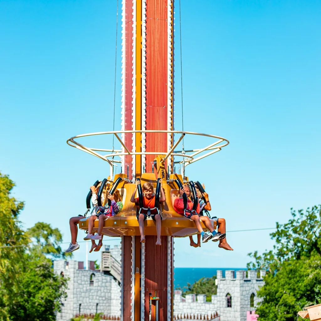 A group of people experiencing the excitement of a drop tower ride at Kneippbyn Gotland under a bright blue sky.