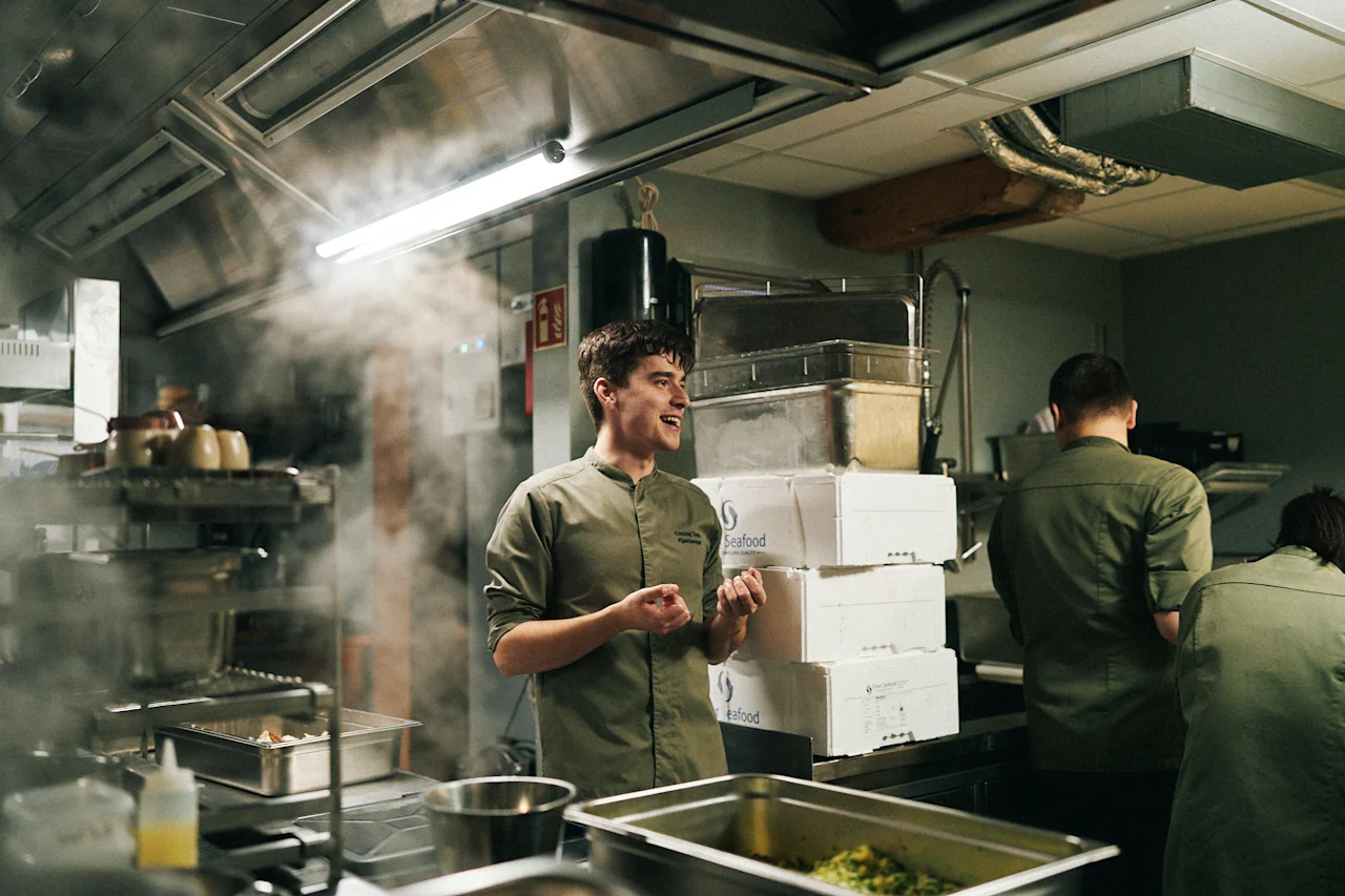 Kokke arbejder i et travlt køkken på Sjøbua, Hotel Brosundet, Ålesund. Damp stiger, mens de tilbereder fiskeretter.