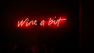 A sign in red light with the text "Wine a bit"