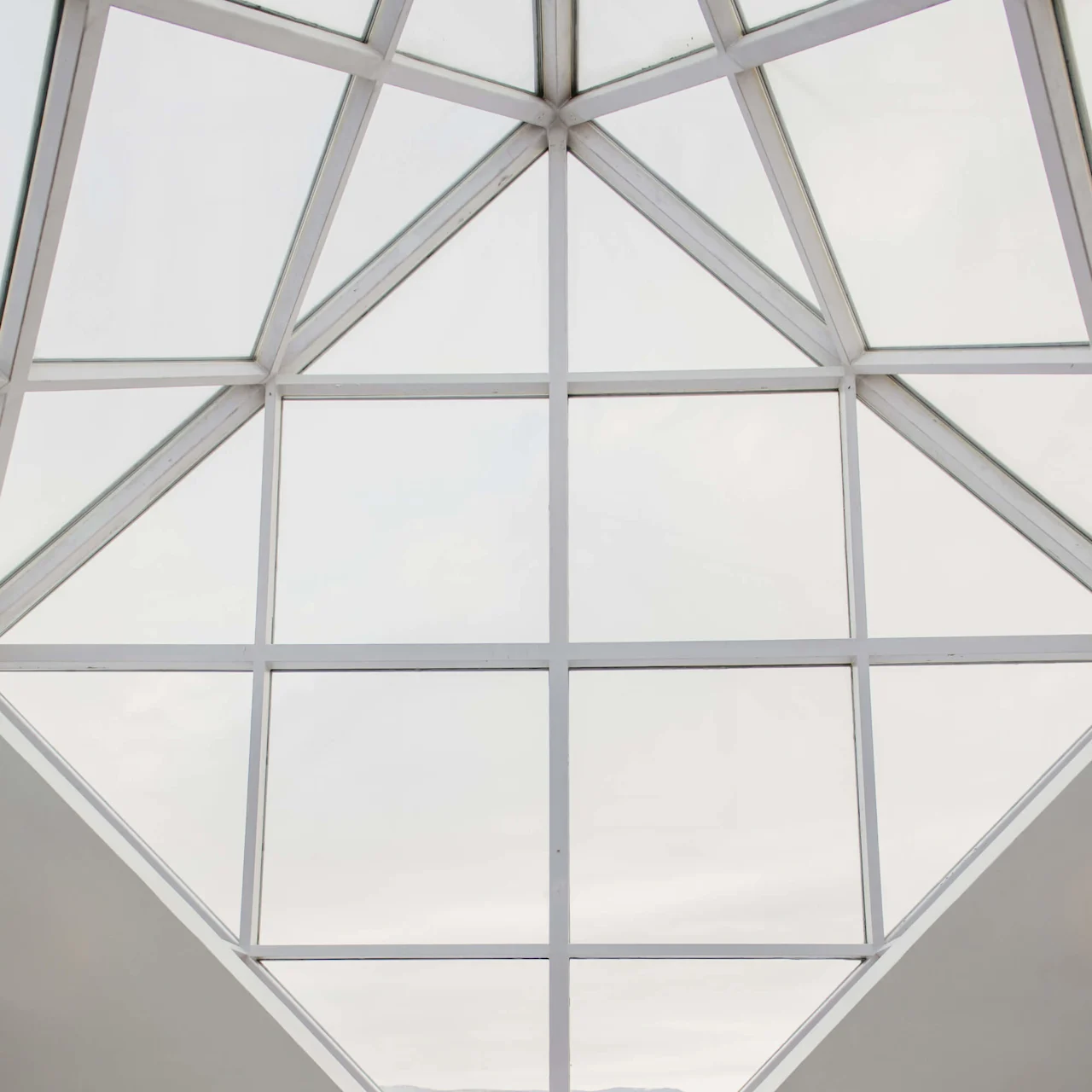Person lying in a geometric window nook, wearing a white robe and towel, relaxing. Surrounding are large glass panes and brown-tiled walls in a spacious indoor area.