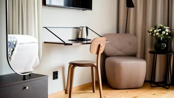 A modern room with a chair, wall-mounted TV, armchair, and side table, with natural light. 