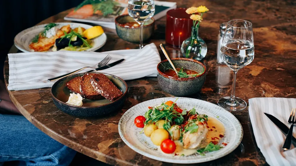 Ett urval av rätter på ett bord dukat för en måltid med glas vatten, antyder en restaurangmiljö.