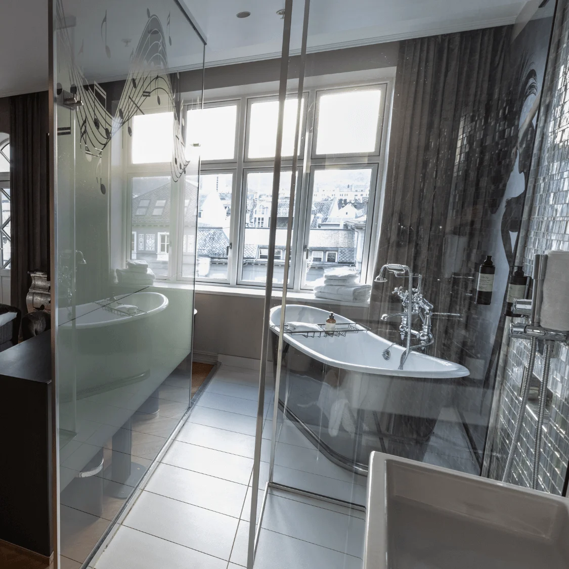 A cozy bedroom features a double bed with purple pillows and a swan mural. Adjacent is a modern glass-walled bathroom with a standalone bathtub, bathed in natural light from large windows.