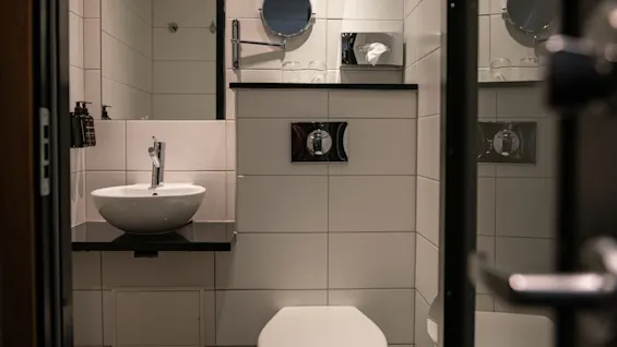 Siisti ja moderni hotellin kylpyhuone, jossa on valkoinen pesuallas, wc ja kaakeloidut seinät. Mukavuuksiin kuuluu peili ja nenäliina-annostelija.