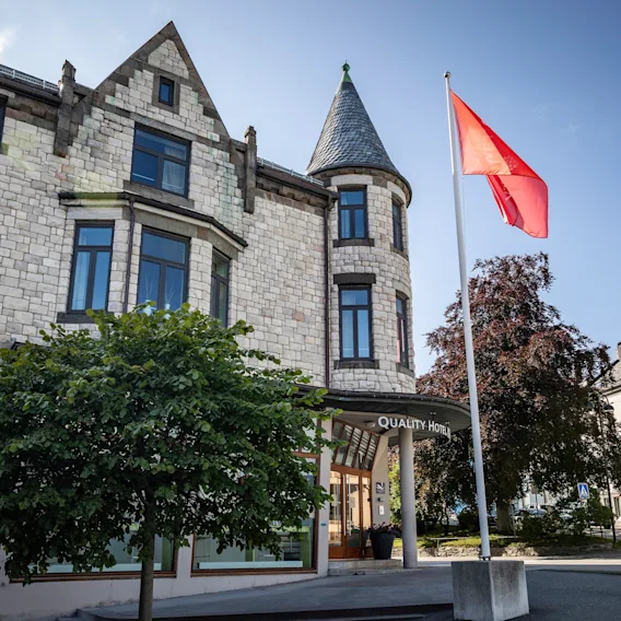 En steinbygning med et tårn og et rødt flagg som vaier. Inngangen har et skilt hvor det står "Hotell".