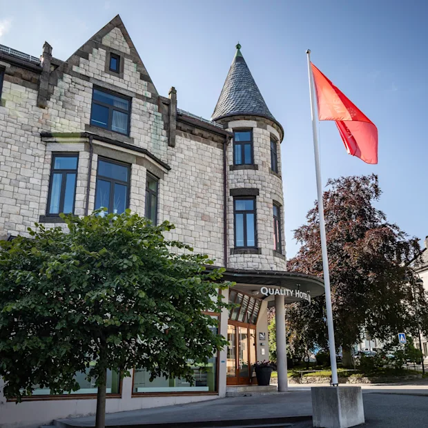 En steinbygning med et tårn og et rødt flagg som vaier. Inngangen har et skilt hvor det står "Hotell".