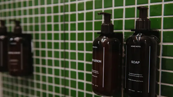 Two dark bottles of LOTION and SOAP mounted on a green tiled wall at Home Hotel Uppsala.