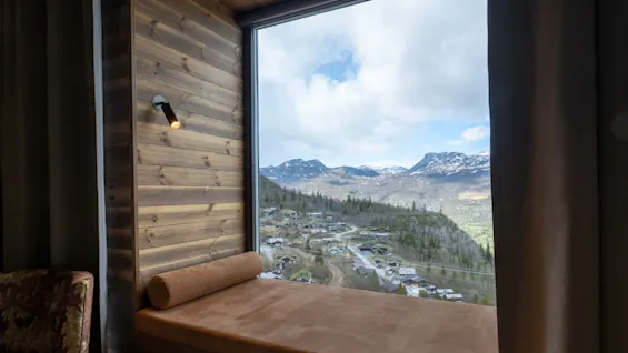 En mysig fönsternisch med en dagbädd erbjuder en fantastisk utsikt över ett bergslandskap och en by nedanför.
