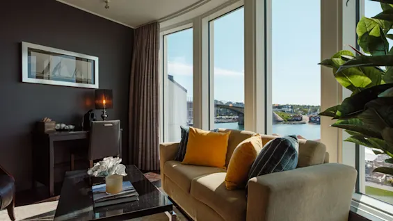 En moderne stue med sofa, sofabord og et stort vindue med udsigt over by, vand og bro.