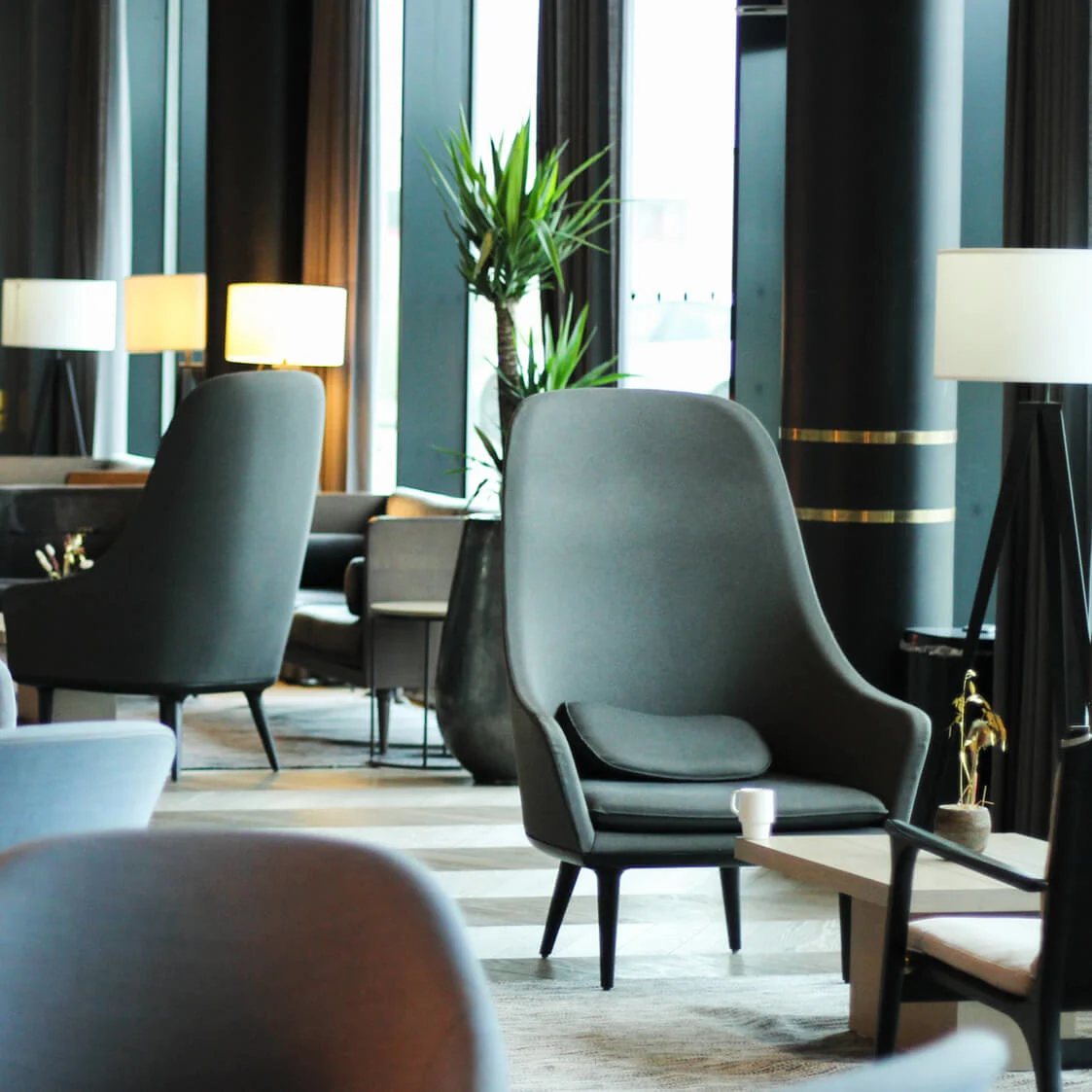 Luksuriøse loungestoler står stille i en moderne hotellobby, omgitt av moderne innredning, potteplanter og myk belysning, som skaper en innbydende og rolig atmosfære.