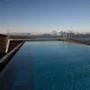 Infinity-pool strækker sig mod glasrækværk, med udsigt over snedækkede bjerge under en klar blå himmel.