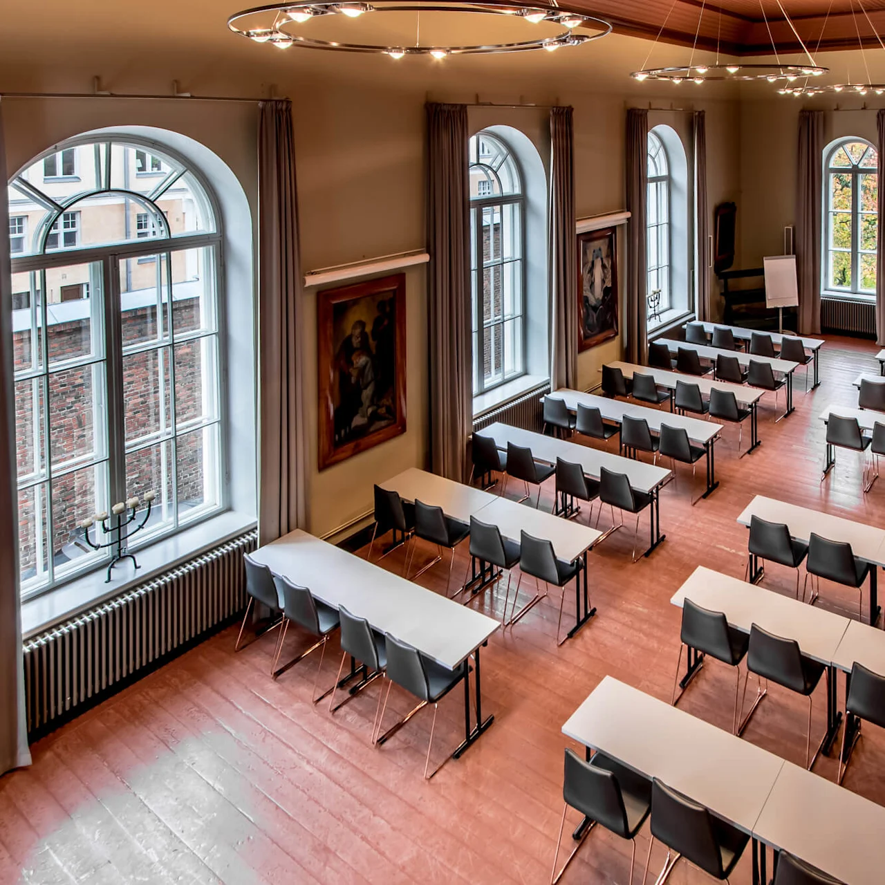 Conference room with arranged tables and chairs, large windows, and artwork on the walls, suggesting an academic or conference setting.