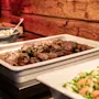 En lækker buffet med en hovedret af kød og en farverig sideret med blandede grøntsager, anrettet mod en rustik træbaggrund.