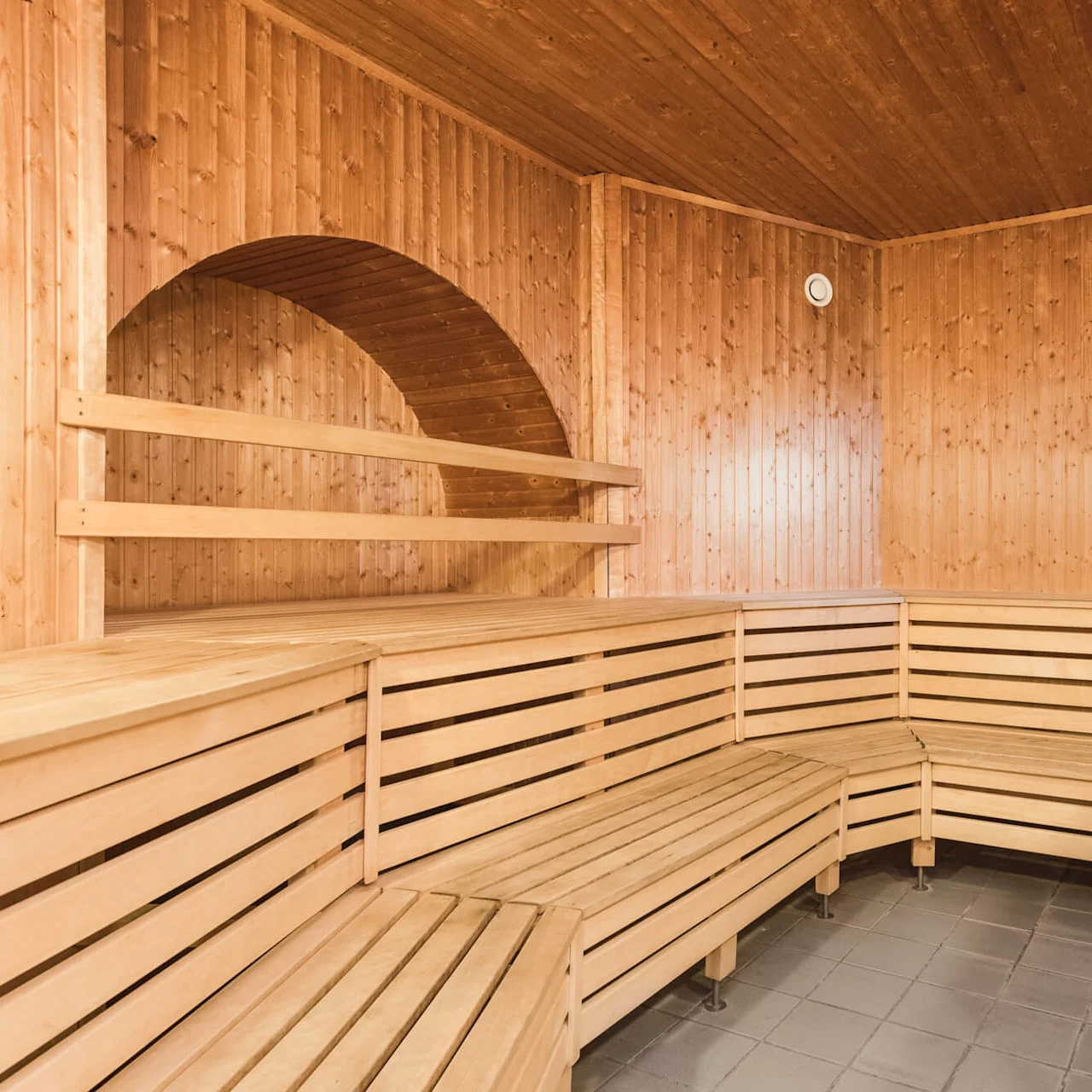 Wooden sauna interior with tiered benches and a heater. Context is a calm, private space.