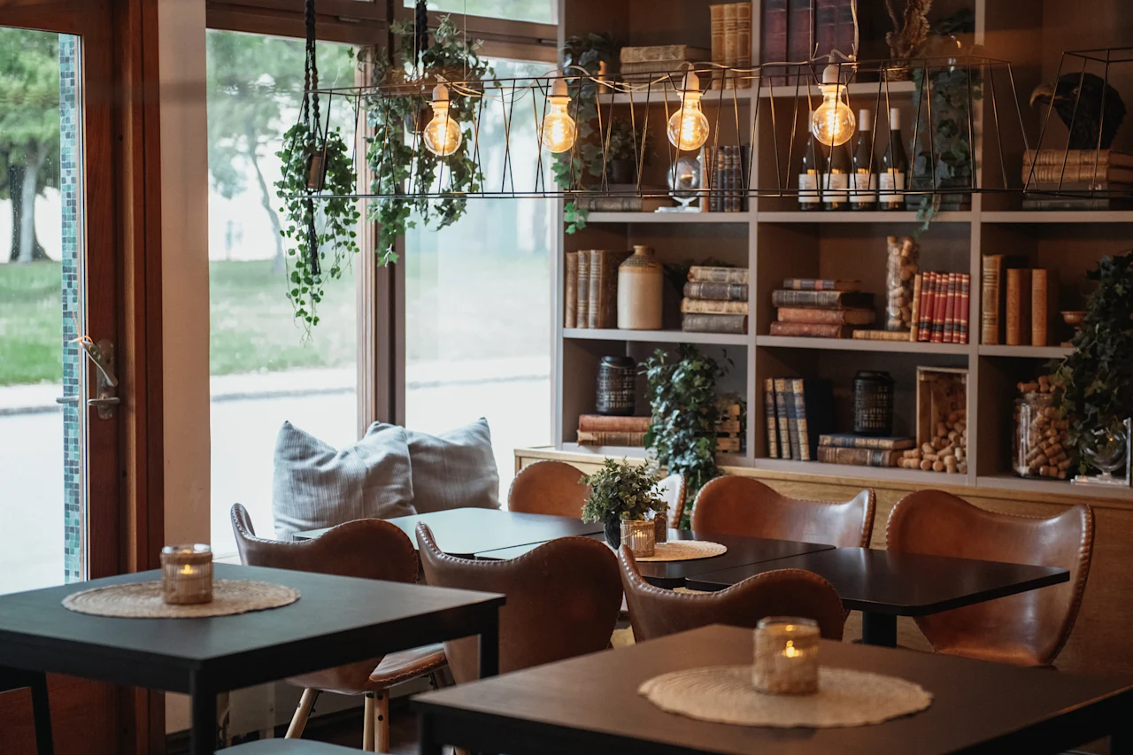 A warm and inviting cafe or lounge area with comfortable seating, soft lighting from candles and hanging bulbs, and a bookshelf.