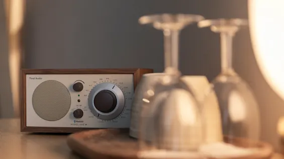 Klassinen Audio-radio, jossa on FM AM, Bluetooth ja MODEL ONE -teksti, kahden viinilasin vieressä puisella tarjottimella, lämpimässä valossa.