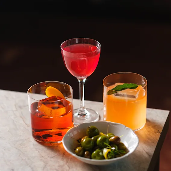A selection of colorful cocktails and a bowl of olives on a marble table, suggesting a social gathering or happy hour.