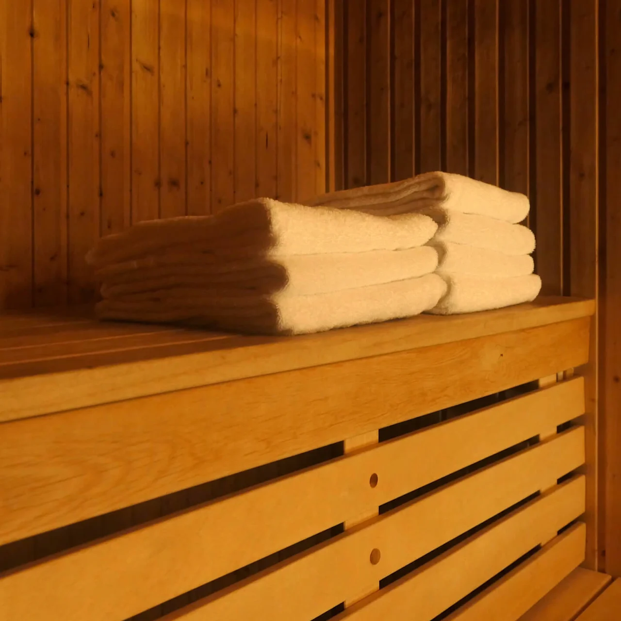 Hvite håndklær er pent stablet på en trek bench inne i en varmt opplyst sauna.