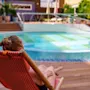 En person slapper af i en rødstribet liggestol ved en rund pool. Miljøet er udendørs med potteplanter og trædæk omkring området.