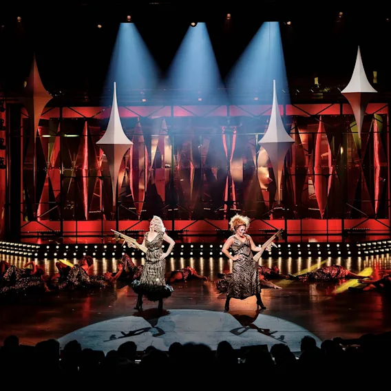 Två artister uppträder på en dramatiskt belyst teaterscen under en stor föreställning.