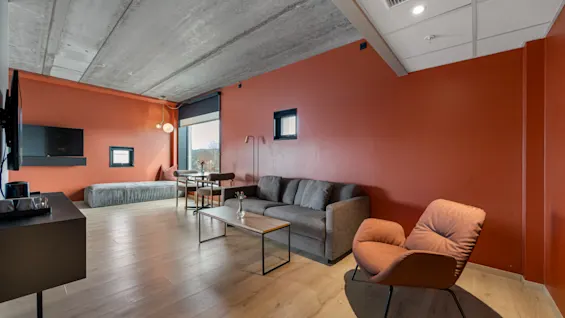 Et moderne og innbydende salongområde med en komfortabel sofa, lenestol, spisebord og et stort vindu som gir naturlig lys.