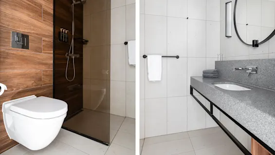Vegghengt toalett, dusj og vask på et moderne bad med lyse fliser og tretone. Minimalistisk design, med et rundt speil og håndklestang.