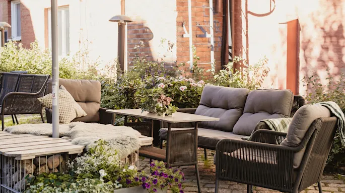 En koselig uteplass med komfortable sitteplasser, et bord pyntet med blomster og frodige grønne planter, perfekt for avslapning.