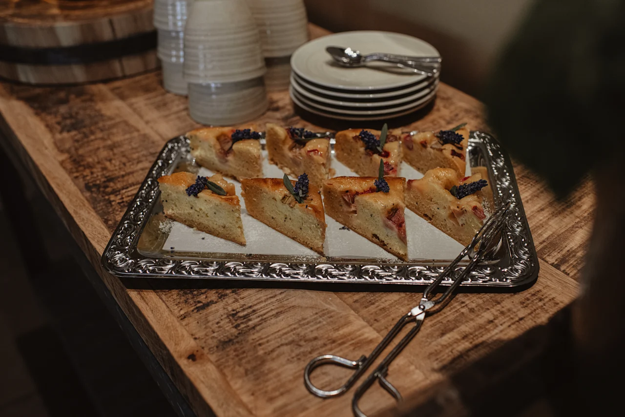 En silverbricka fylld med vackert garnerade tårtbitar, redo att serveras, med tallrikar och bestick i bakgrunden.