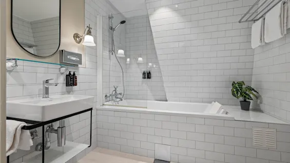 A clean and modern bathroom featuring white subway tiles, a sleek sink, a bathtub with a shower, and fresh towels.