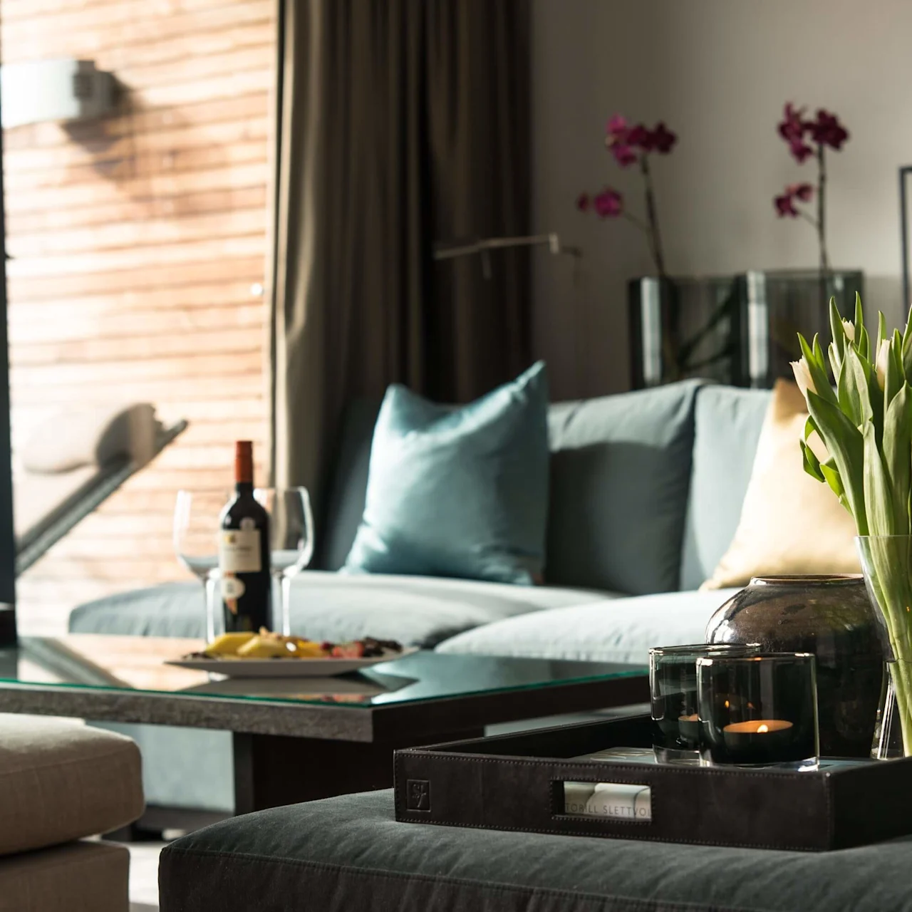 Et moderne stue med en blå sofa, puder, en vase med tulipaner på et bord, og sløret vin og frugtfad.