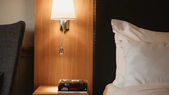 A cozy bedside scene with a lamp, books on a nightstand, and a comfortable bed, perfect for relaxing or reading.
