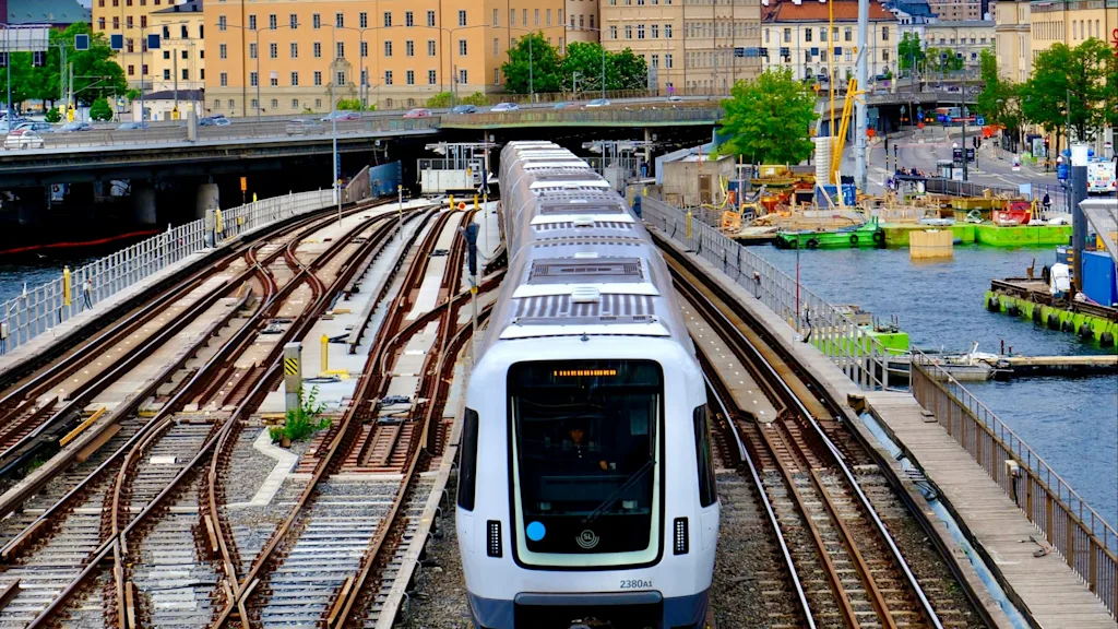En tunnelbana i Stockholm, tåg 2380A1, stadssilhuett och vatten i bakgrunden.