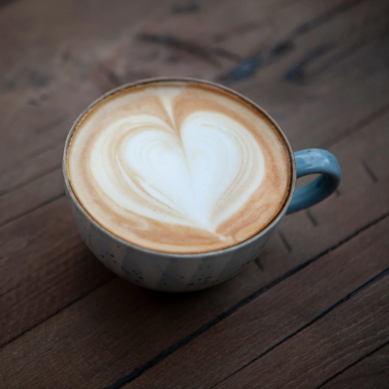 En cappuccino-kopp med hjerteformet lattekunst står på et trebord, og tilfører en varm, kunstnerisk touch til en koselig setting.