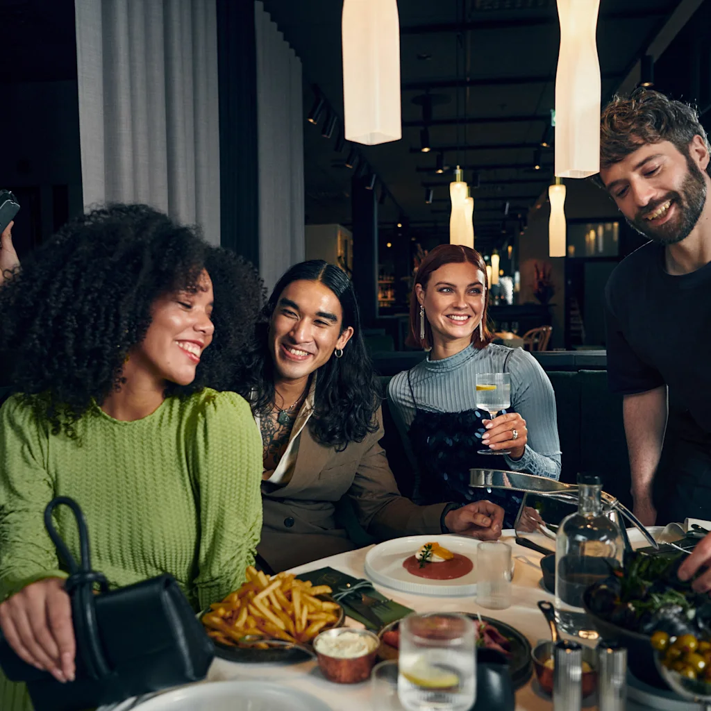Clarion: Friends laughing and sharing a meal at a vibrant restaurant, with a server presenting delicious dishes.