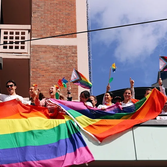 En gruppe mennesker som står på en balkong og vifter med Pride-flagg