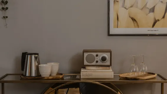 En mysig hotellrumsinredning på Home Hotel Grand, Helsingborg, med en vattenkokare, koppar, en radio på böcker inklusive SYMBOL LEXIKONET och vinglas på ett konsolbord.