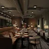 Lyxig lounge med mjuka sittplatser; bord dukade med tallrikar och glas; mysig atmosfär med mjuk belysning; dekorativa inslag inkluderar växter och en öppen spis i en modern, exklusiv miljö.