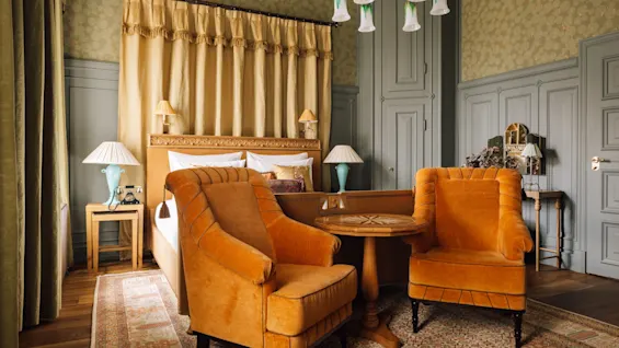 Elegant interiør med to oransje lenestoler, bord, klassisk dekor; sofistikert viktoriansk atmosfære.