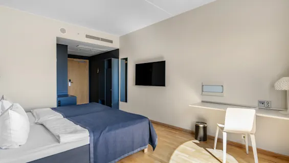 Et moderne hotelværelse med to senge, et vægmonteret TV og et skrivebordsområde med stol, klar til arbejde eller afslapning.
