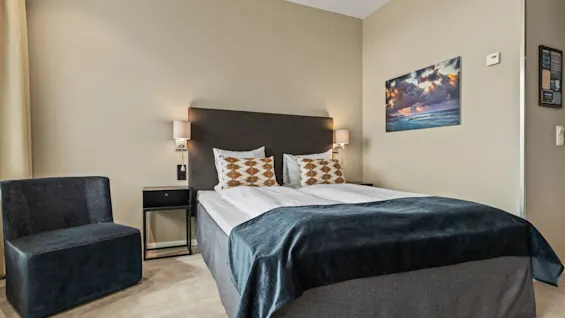 Ett bekvämt hotellrum på Quality Hotel Ulstein med en stor säng, mysig fåtölj och ett naturskönt konstverk på väggen.