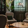 A cozy lounge area at Home Hotel Uppsala with two armchairs, a wooden coffee table, a plant, and a decorative floor lamp.