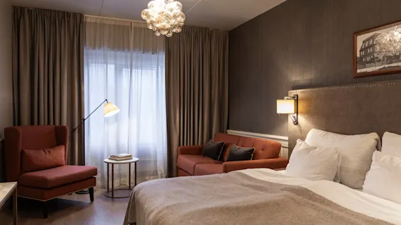 A welcoming hotel room at Home Hotel Grand Bodø featuring a comfortable bed, a sofa, and an armchair with warm lighting.