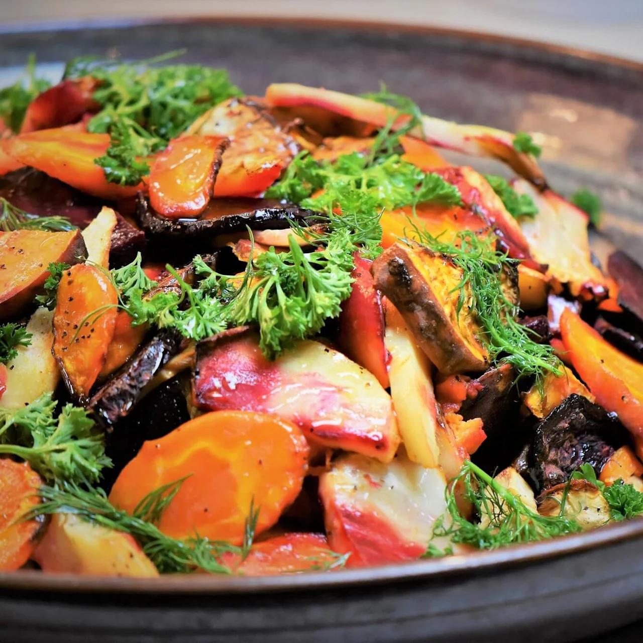 A colorful roasted vegetable dish in a dark bowl, garnished with fresh herbs.
