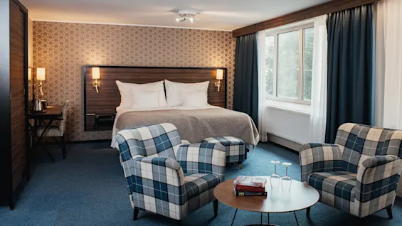 Kutsuva hotellihuone, jossa on mukava sänky, ruudulliset istuimet ja työpöytä, täydellinen rentoutumiseen tai työskentelyyn.