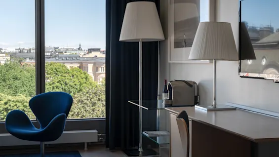A modern hotel room at Clarion Hotel Sign with a city view, featuring a blue armchair and a desk area.