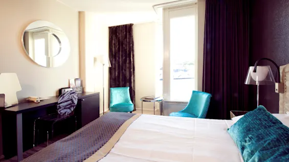 A neatly made bed in a well-lit hotel room with modern furnishings and blue accents.