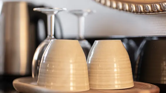 Kaksi keraamista kuppia ja kaksi viinilasia on aseteltu viihtyisästi puutarjottimelle, kutsuen virkistävään hetkeen.