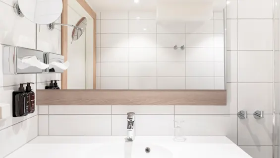 Et lyst, moderne baderom med hvit vask, stort speil og toalettartikler, klart til bruk.