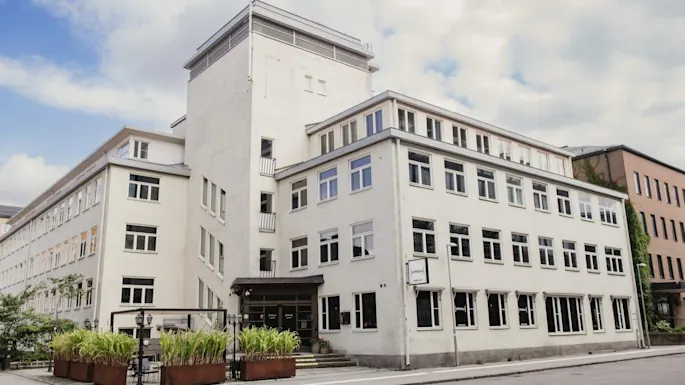 Eksteriør av en hvit hotellbygning med 'home hotel'-skilt, grønne planter og en gate foran. Home Hotel Uppsala.