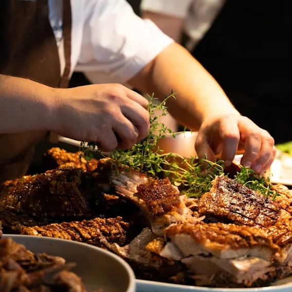 En kokk anretter et kjøttmåltid med friske urter på et restaurantkjøkken.